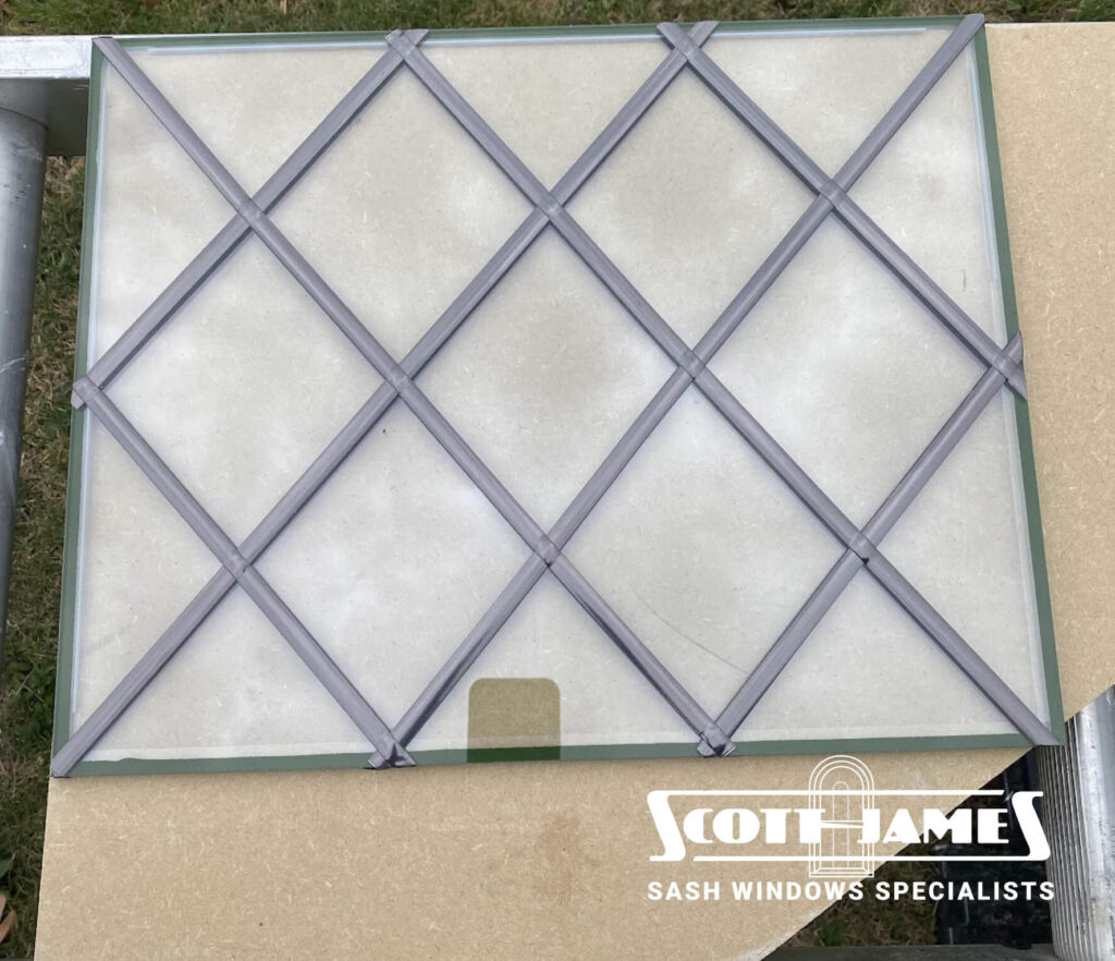 vacuum double glazing  with a diamond grid pattern, hinting at classic leaded windows, rests on a cardboard surface. The logo "Scott James Sash Windows Specialists" is visible in the bottom right corner, showcasing expertise in double glazing retrofitting.