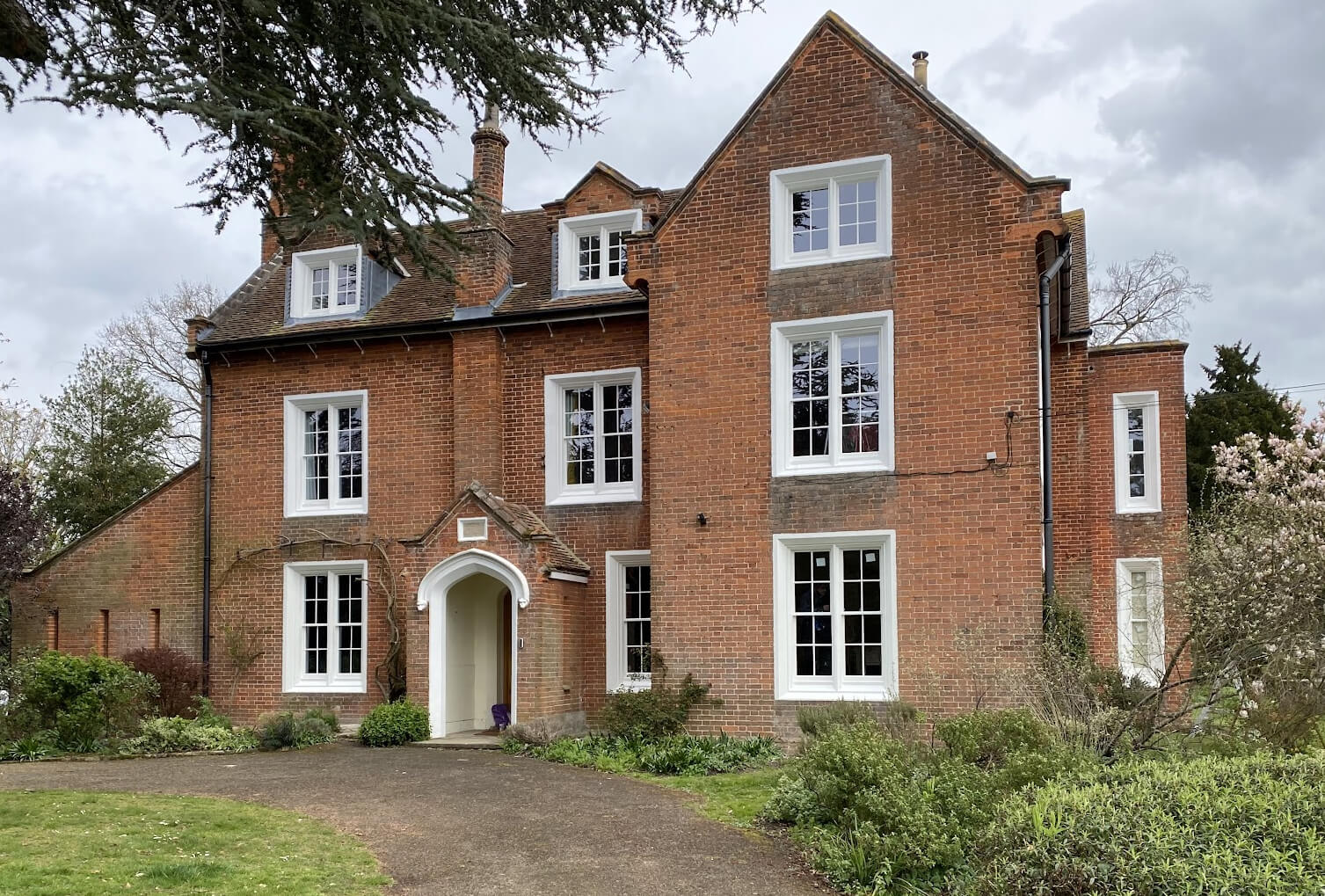 A large red brick house in the middle of a garden, retrofitted with double-glazing.