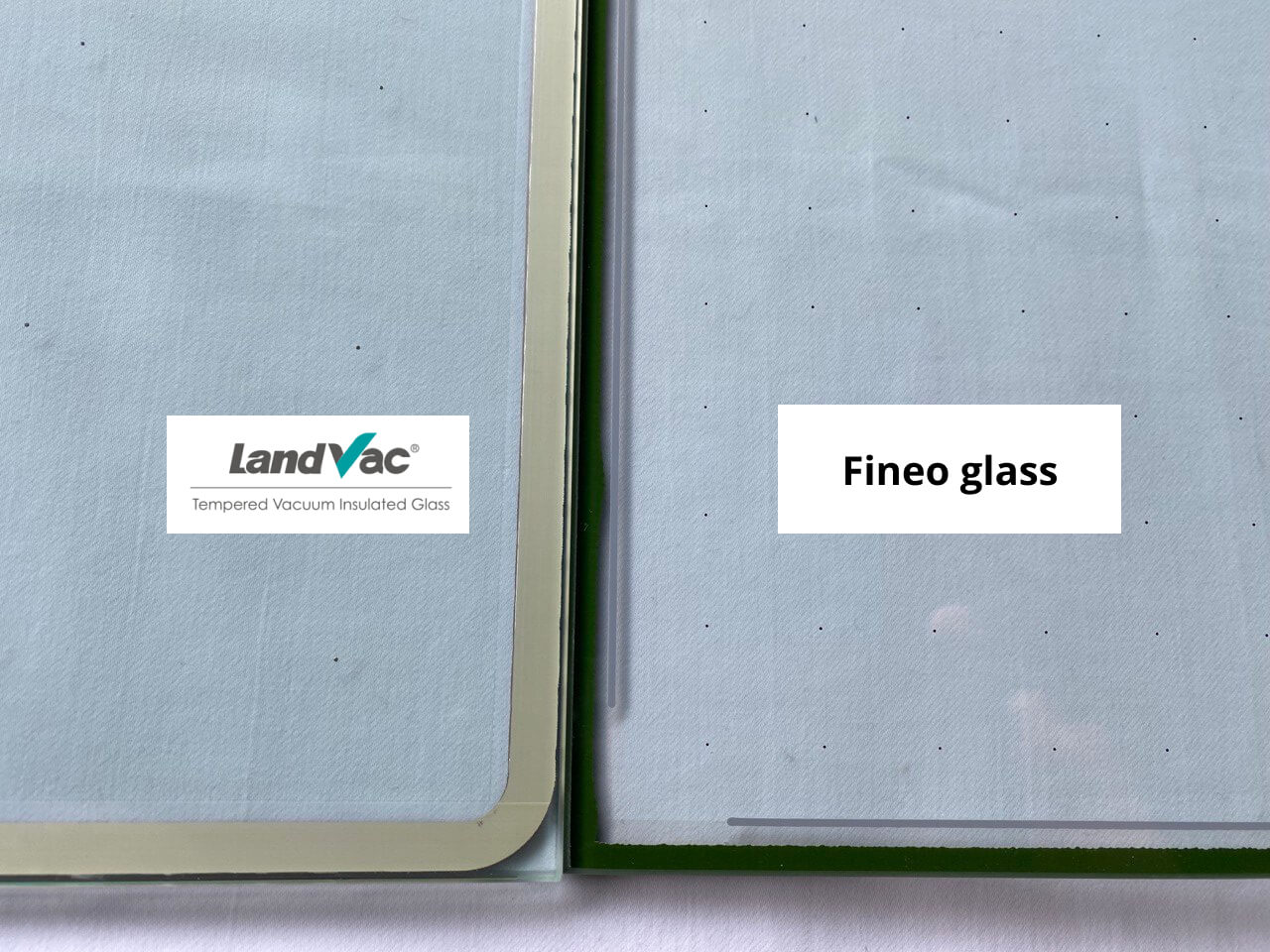 Two glass panels stand side by side, labeled "LandVac Tempered Vacuum Insulated Glass" and "Fineo glass," showcasing a comparison between LandVac vs. Fineo glass, with their protective films partially visible.