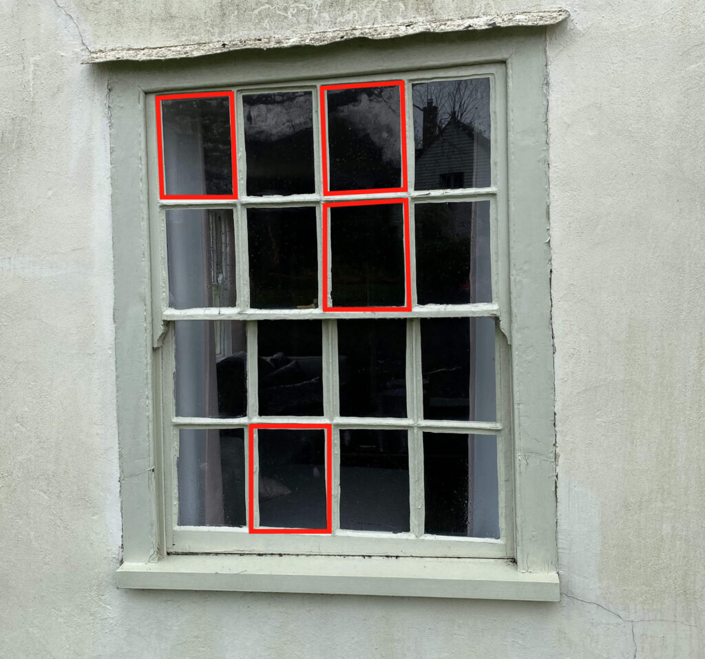 A window with a pale green frame, reminiscent of Georgian sash windows, features multiple glass panes. Five panes are highlighted with red rectangles. The surrounding wall is painted a light gray color.