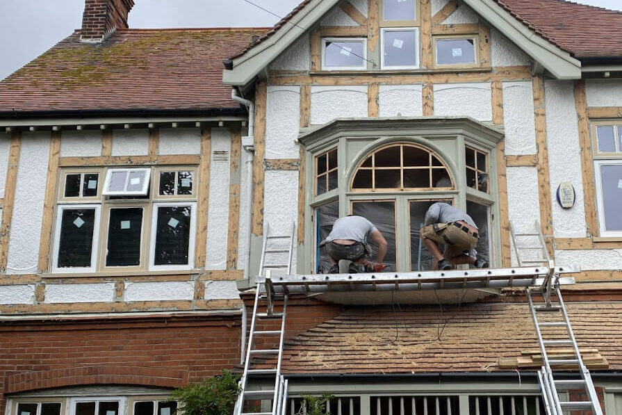 A man on a ladder on top of a house, installing double glazing.