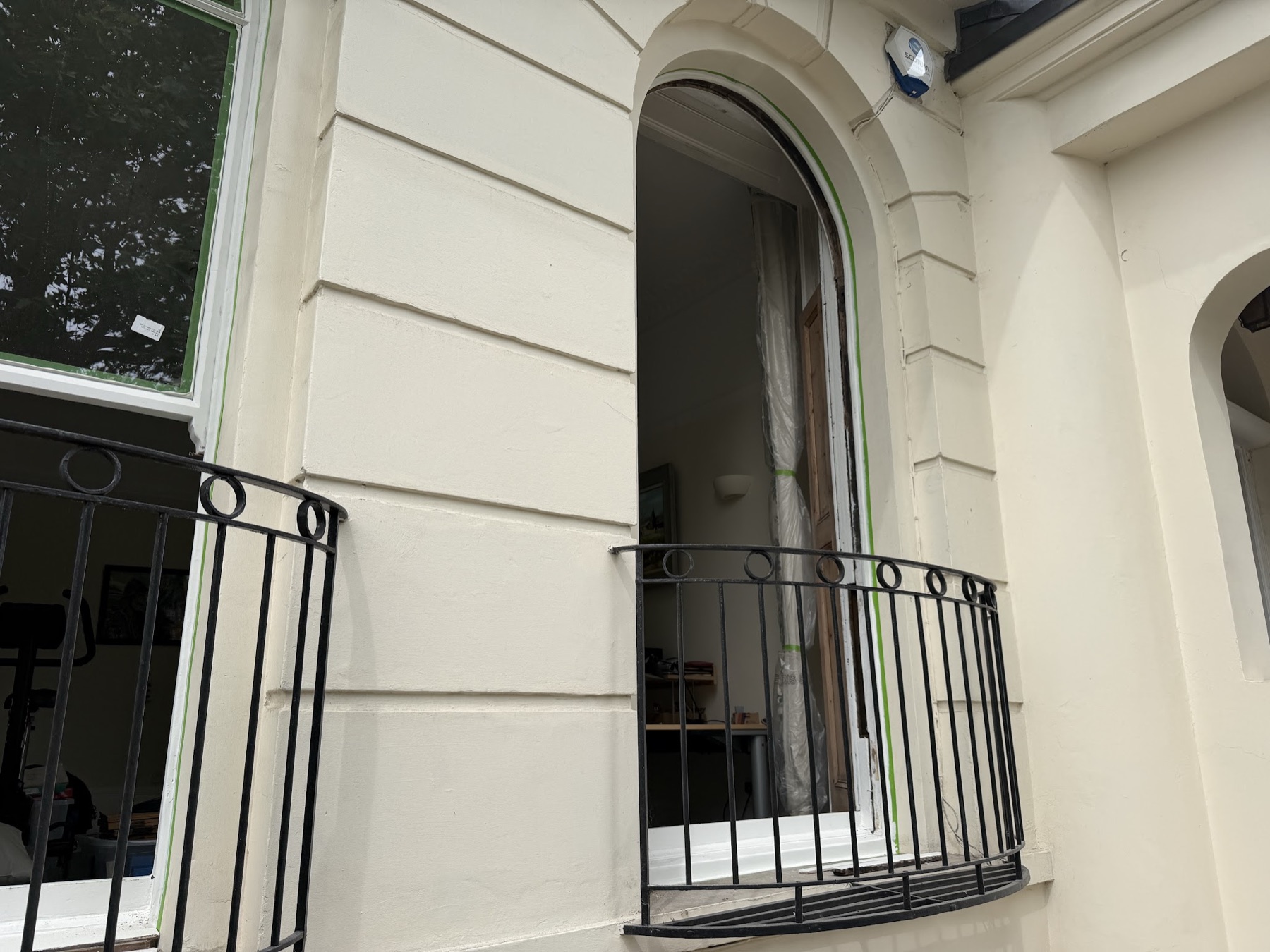 Arched sash window opening during the work, the sash out for reglazing and masking tape on the freshly decorated stucco surround
