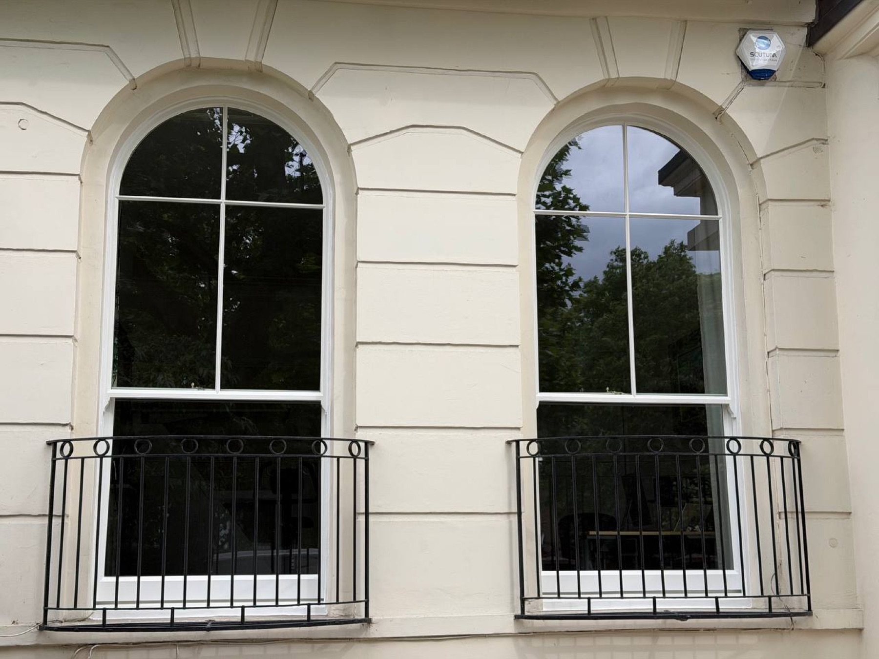 Two round-headed arched sash windows in the stucco ground floor reglazed with LandVac vacuum units, behind curved iron balconettes