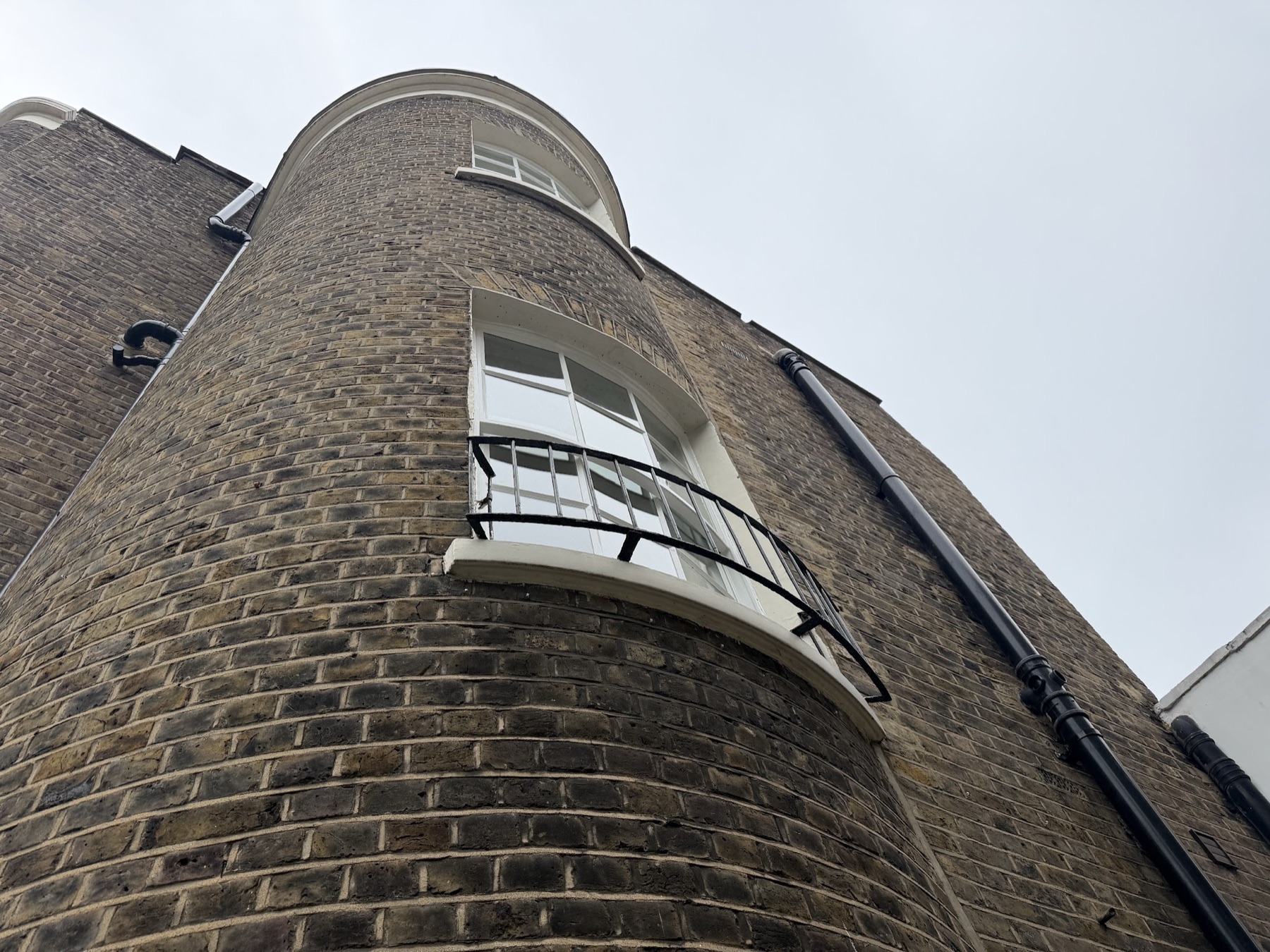 Looking up the curved brick bay: curved sash windows on two floors reglazed with vacuum glass that follows the curve, with a small iron balcony rail