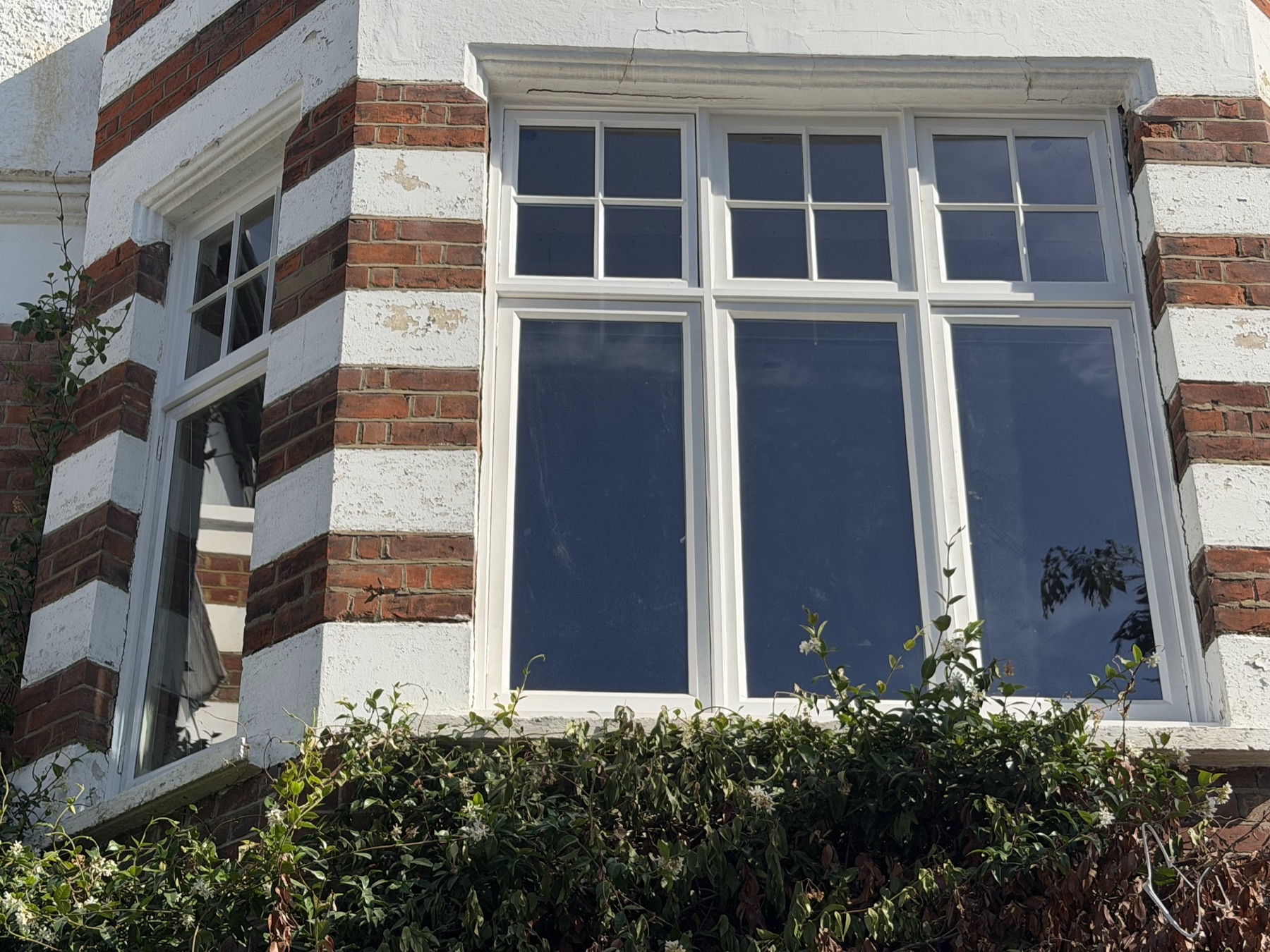 First-floor canted casement bay after reglazing with toughened vacuum units, six-pane top lights over tall single panes, red brick and render banding