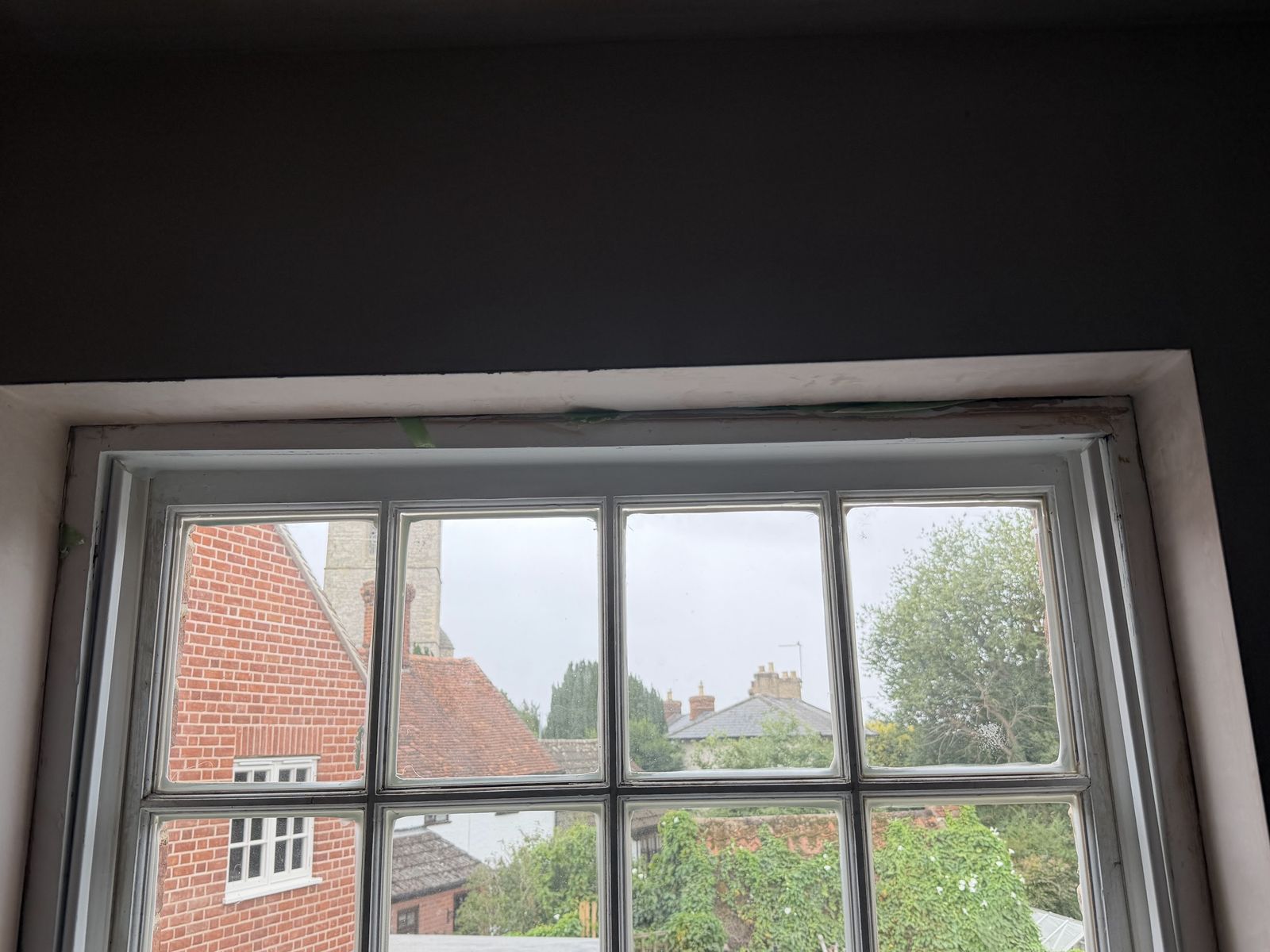 Old six-pane sash window with worn beads and gaps at the head before draught proofing