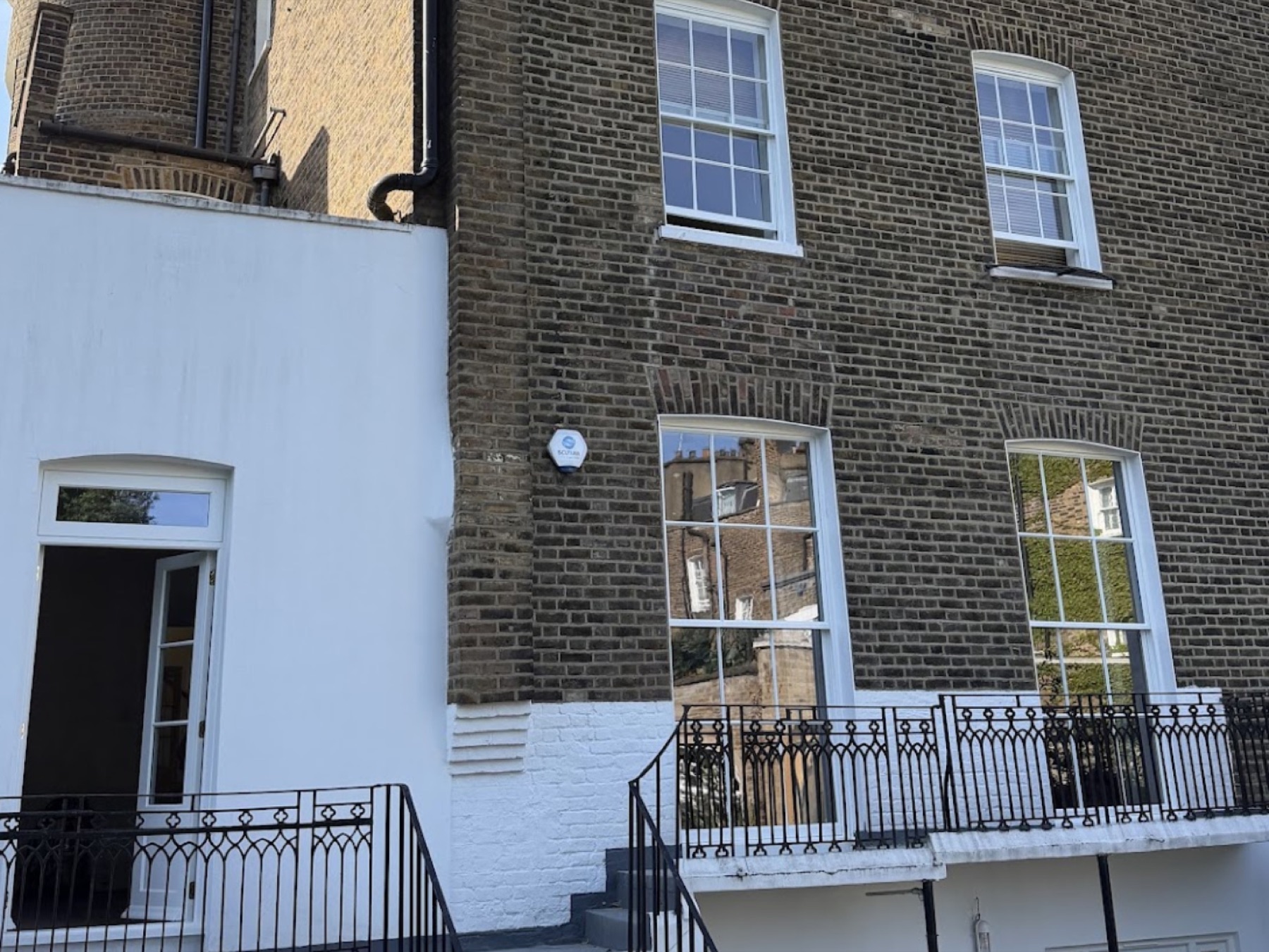 Rear elevation after the work: restored sash windows in the brick upper floors above the white rendered garden level and its French door